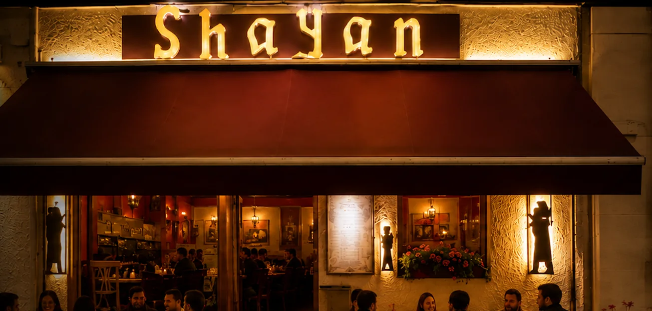 Restaurant Shayan bei Nacht: beleuchteter Schriftzug über der Fassade, Gäste an Tischen auf dem Gehweg