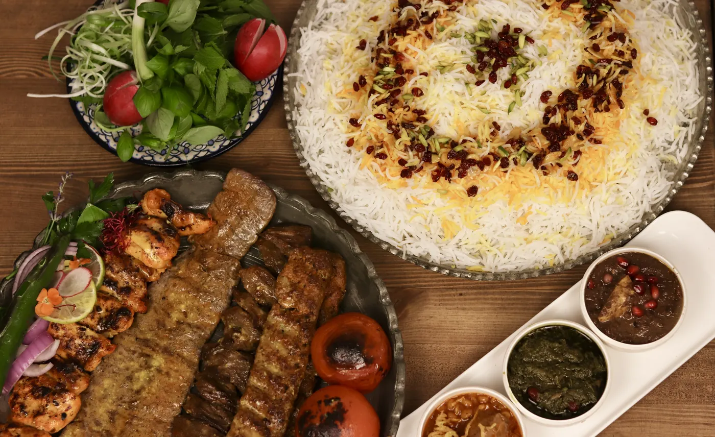 Persische Tafel auf Holz mit Kabab-Spießen, Safranreis, frischem Salat und Dips